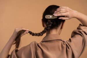 Donna di spalle che regge la sua treccia di capelli scuri, alla base della quale si trova uno degli accessori per capelli più belli e adatti per un look sempre attuale.