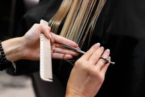Foto delle mani esperte di una parrucchiera intenta a tagliare i capelli biondi di una donna.