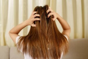 Immagine che mostra una donna vista di spalle mentre solleva i capelli con entrambe le mani, rivelando il cuoio capelluto. I capelli appaiono spenti e con le punte secche e danneggiate, suggerendo la necessità di trattamenti ristrutturanti. Questa situazione è emblematica delle condizioni dei capelli che richiedono un'intensa cura ristrutturante e l'uso di nutrienti maschere per capelli danneggiati per ripristinare la salute e la vitalità della chioma.