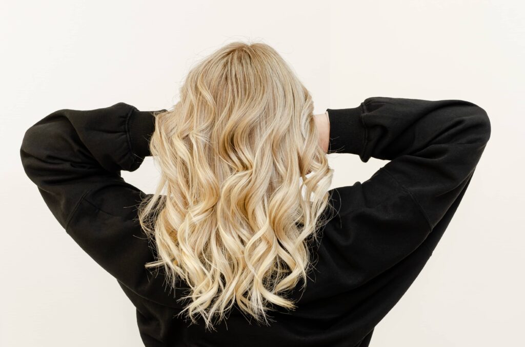 Ragazza bionda con capelli scalati lunghi e ondulati che tiene le braccia sollevate con le mani sul cuoio capelluto.