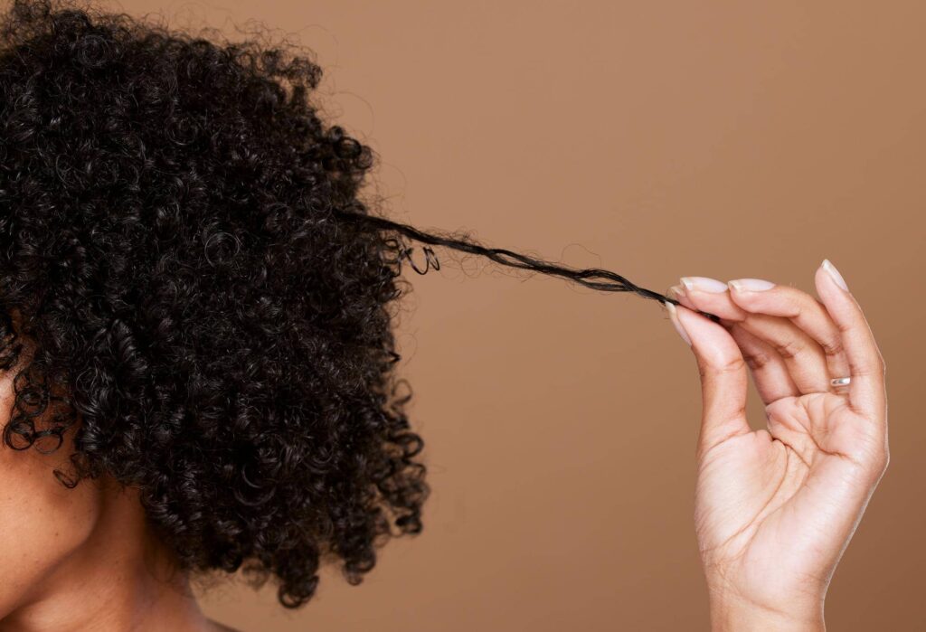 La mano di una donna tiene delicatamente l'estremità di un suo riccio, illustrando la naturale spirale e la texture dei capelli ricci. Questa immagine cattura l'essenza di questo tipo di chioma, sottolineando l'importanza di scegliere prodotti di cura adeguati per mantenere i ricci definiti e ben nutriti, come ad esempio uno shampoo per capelli ricci.