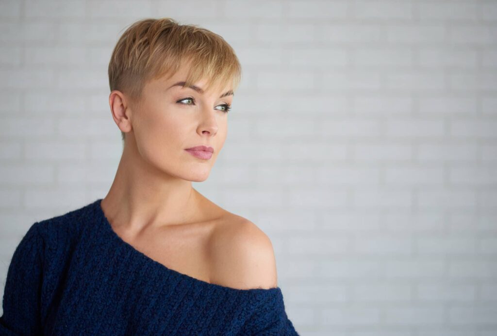 Donna con capelli chiari con un taglio corto pixie cut che guarda in lontananza con atteggiamento sicuro di sé.
