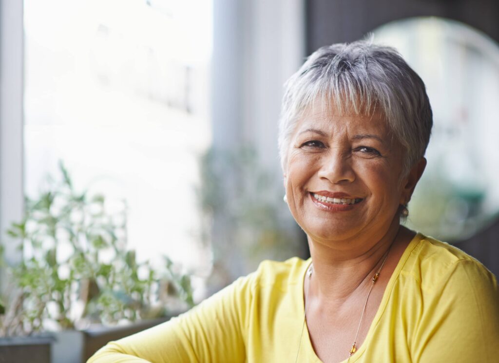 Sorridente donna matura con capelli grigi tagliati in un pixie cut in un ambiente domestico. Ha scelto per il suo stile uno dei migliori tagli di capelli che ringiovaniscono.