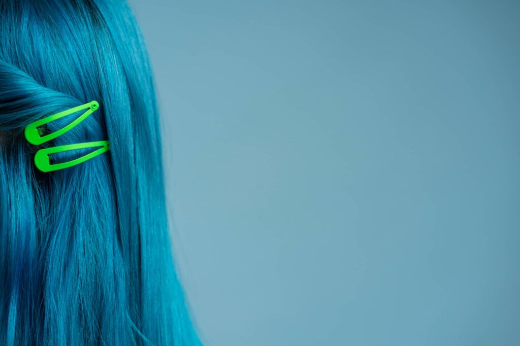 Primo piano di una chioma liscia di colore azzurro adornata da due fermagli a clip verdi.