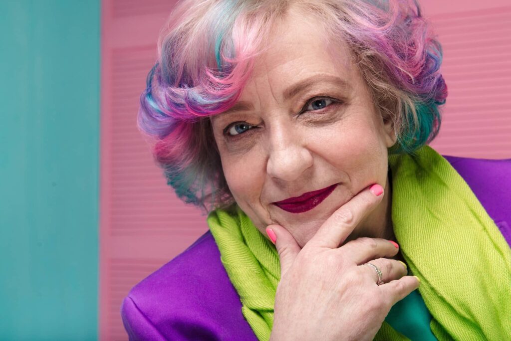 Donna matura pensierosa con capelli grigi con le punte colorate di varie sfumature di azzurro e rosa. Si tratta di una particolare scelta di colore di capelli per sembrare giovane.