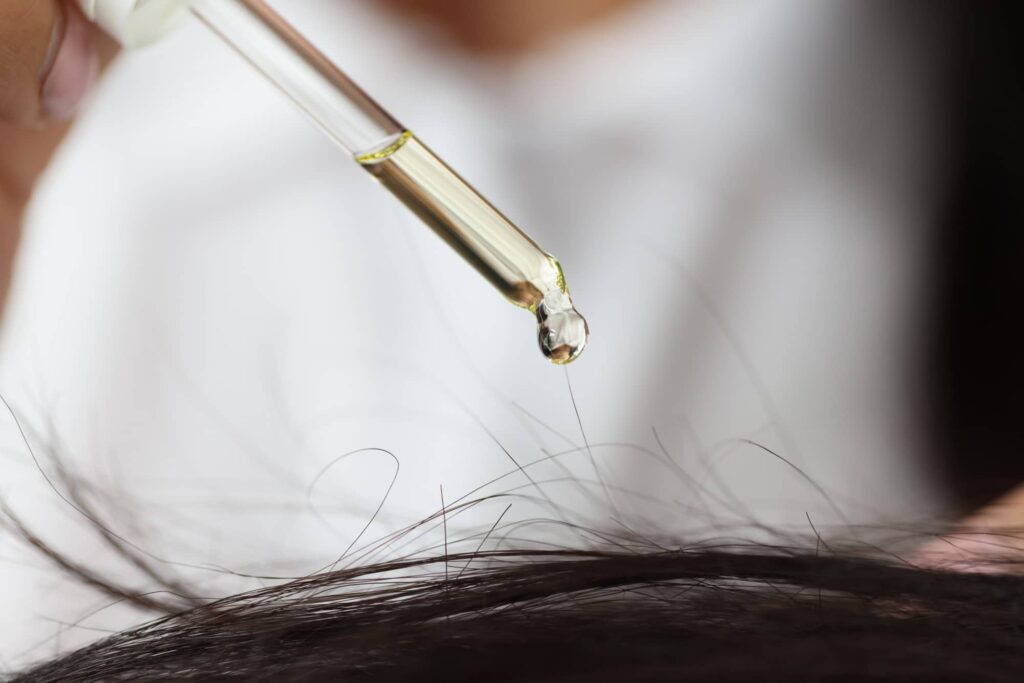 Contagocce che lascia cadere una goccia di trattamento di ricostruzione dei capelli su una chioma castana e liscia.