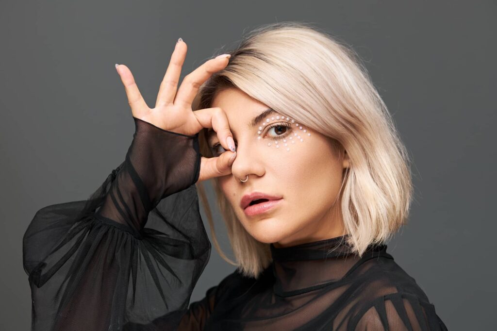 Donna bionda con capelli tinti di media lunghezza che fa il segno “ok” con le dita. Il suo è un taglio di capelli da donna molto popolare.