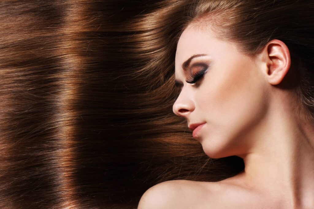 Donna distesa con i capelli castani lunghi e lucenti allargati in orizzontale alle sue spalle, forse dopo aver applicato un trattamento di laminazione ai capelli.