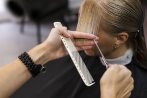 Foto delle mani esperte di una parrucchiera che taglia i capelli biondi di una donna. La cliente si è prima informata per sapere quando tagliare i capelli.