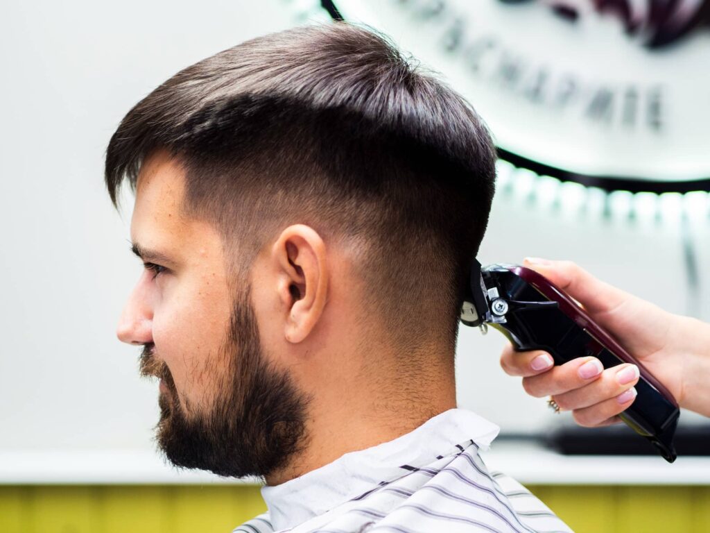 Foto della mano esperta di un parrucchiere che applica uno dei tagli di capelli da uomo con sfumatura più popolari alla capigliatura di un cliente.
