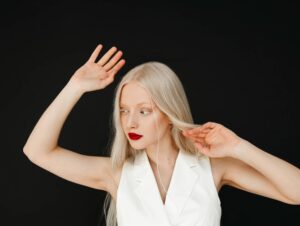 Donna albina con lunghi capelli lisci e fini che guarda di lato con le braccia leggermente sollevate. Sfoggia il miglior taglio per capelli fini per valorizzare al meglio la sua figura.