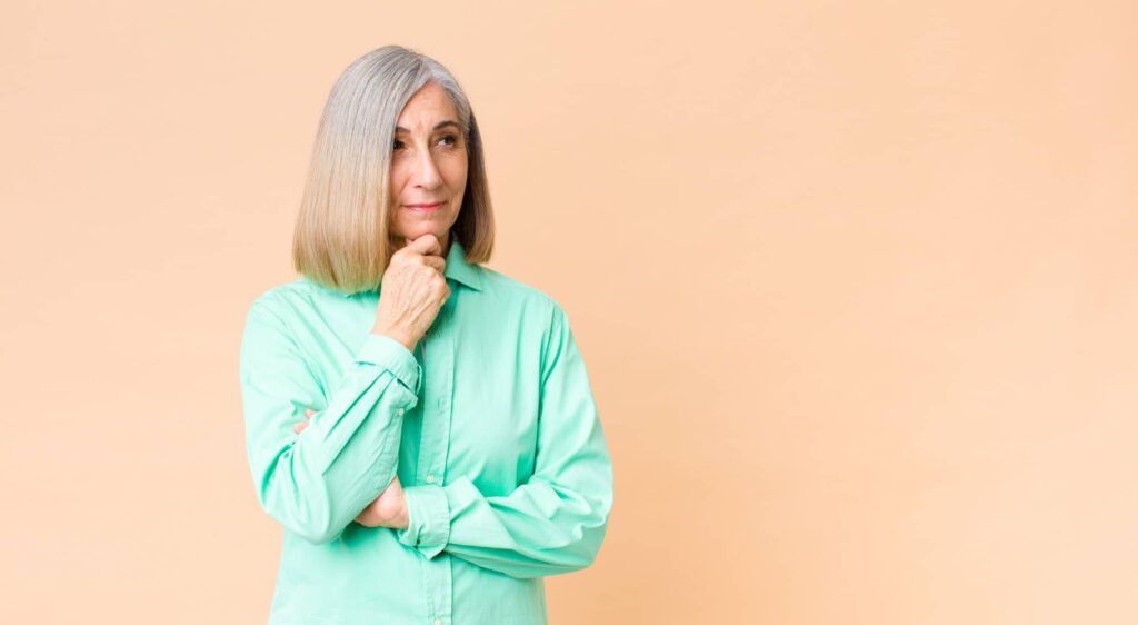 Donna matura con lunghi capelli sfumati dal grigio al biondo con espressione pensierosa. Ha scelto il miglior colore di capelli a 60 anni per esprimere la sua personalità.