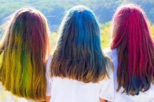 Foto di tre ragazze di spalle con i capelli lunghi multicolori e un paesaggio naturale sullo sfondo.