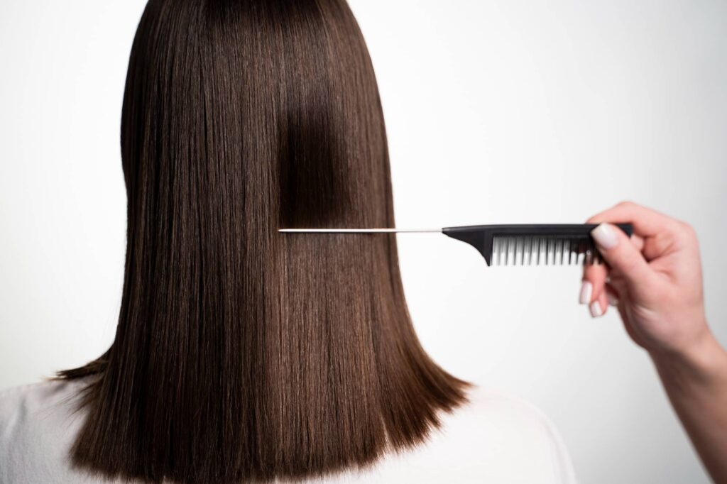 Una persona con capelli lisci e lucenti, trattati con shampoo alla cheratina, viene pettinata con un pettine largo. L'immagine mostra capelli ben curati e sani, risultato dell'uso di prodotti di qualità come shampoo per la crescita dei capelli e il loro rafforzamento.