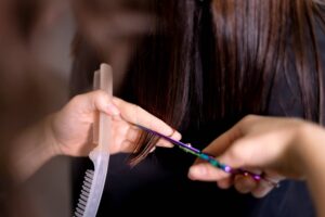 Foto delle mani esperte di una parrucchiera che tagliano la chioma castana di una donna. La cliente aveva chiesto quando tagliare i capelli per farli crescere più velocemente.