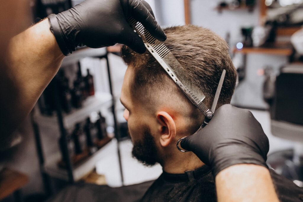 Foto delle mani esperte di un parrucchiere che taglia i capelli castani di un giovane uomo per modellarli in un taglio di capelli corto. Il cliente ha saputo riconoscere il momento giusto per un taglio grazie alle sue conoscenze sulla durata di un taglio di capelli da uomo.
