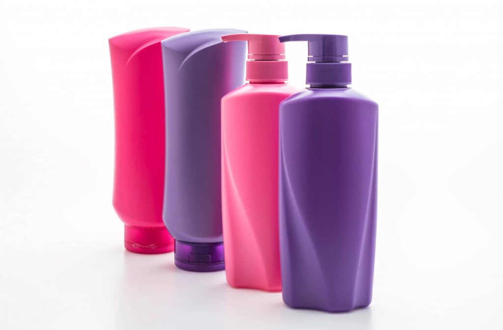 Quattro flaconi di shampoo colorante di alta qualità in fila, con tonalità vivaci che vanno dal fucsia al viola. I contenitori mostrano diversi design e tappi a pompa per un utilizzo facile e pratico, suggerendo una varietà di opzioni per colorare e trattare i capelli.