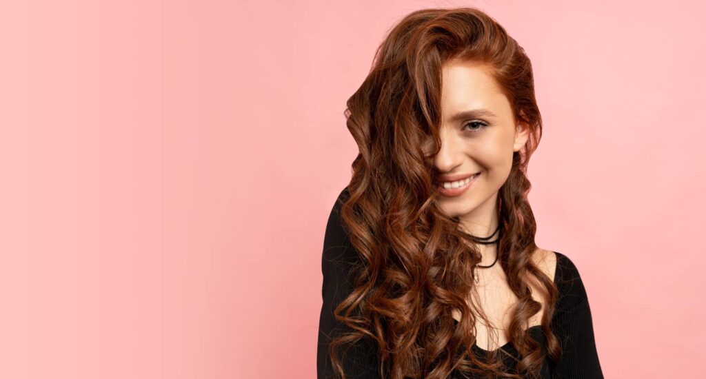 Ragazza sorridente con i lunghi capelli ondulati che le coprono parte del viso. porta con stile ed eleganza uno dei migliori tagli per capelli mossi disponibili.