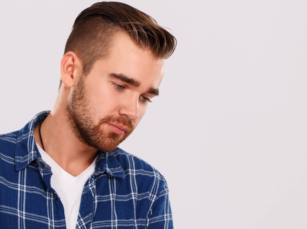 Giovane uomo con barba e lisci capelli castani, più corti sui lati e lunghi in cima alla testa, in linea con un taglio di capelli da uomo molto in voga.