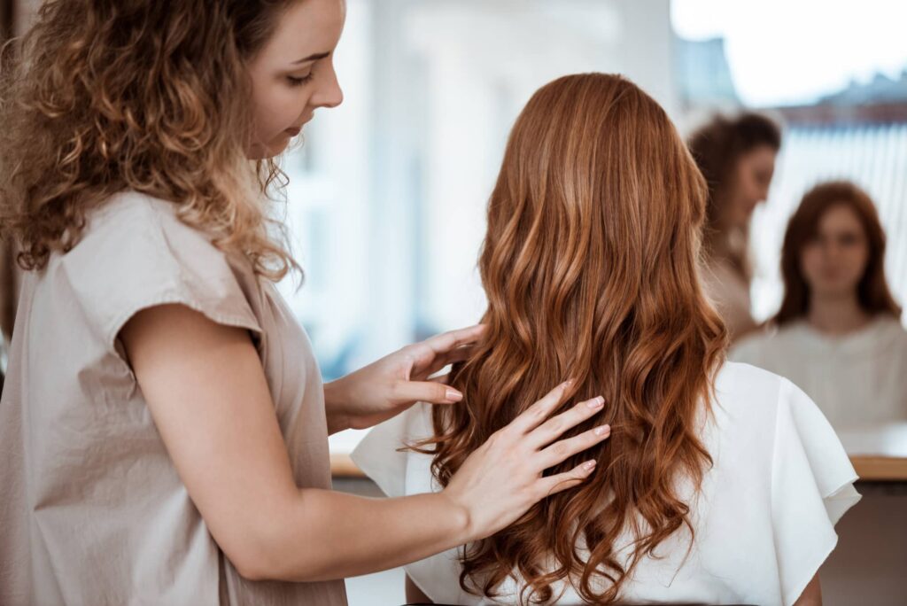 Una parrucchiera esperta accarezza i lunghi capelli castano chiaro di una cliente per sistemarli al meglio.