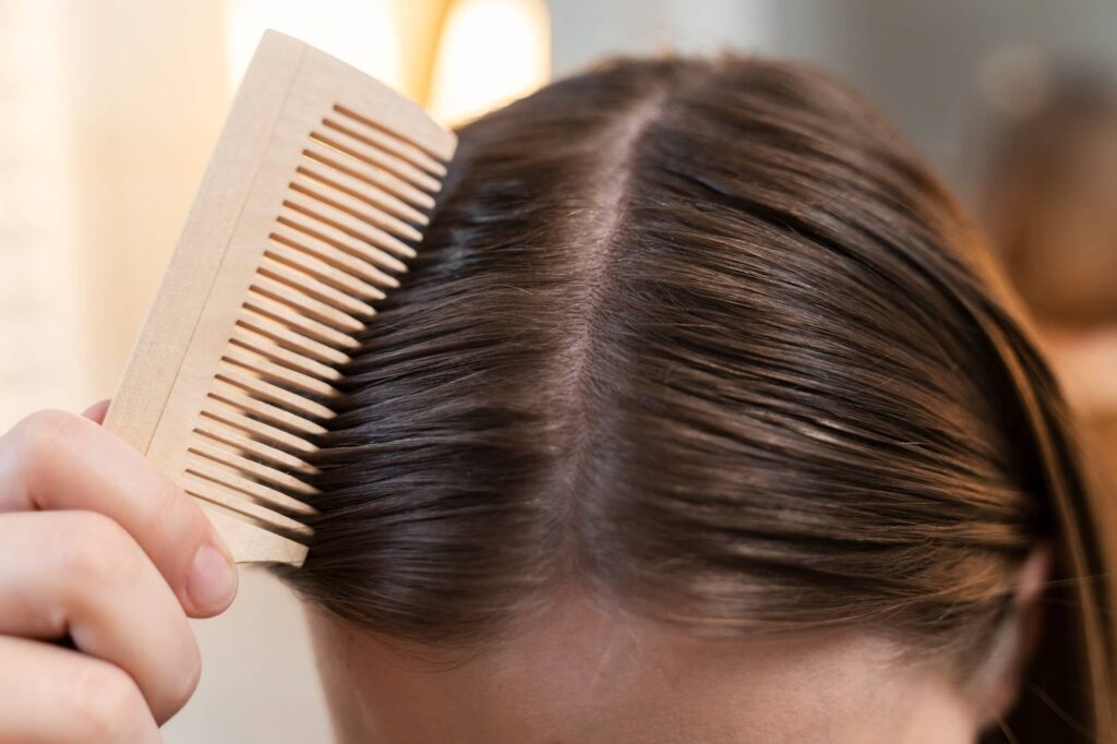 Foto dall’alto della testa di una ragazza che si pettina i lisci capelli grassi castani. Probabilmente ha bisogno di prodotti per capelli grassi.