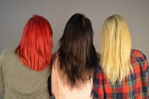 Foto di tre ragazze di spalle con i capelli lunghi di tre colori diversi. Da sinistra verso destra: rosso acceso, castano scuro, biondo oro.