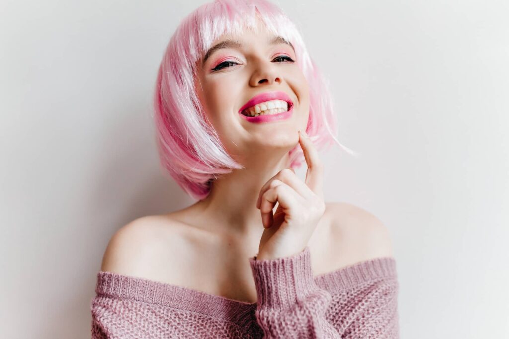 Ragazza felice che indossa una parrucca rosa. La sua felicità è dovuta al fatto che le parrucche ti consentono di cambiare stile in modo facile, veloce e temporaneo.